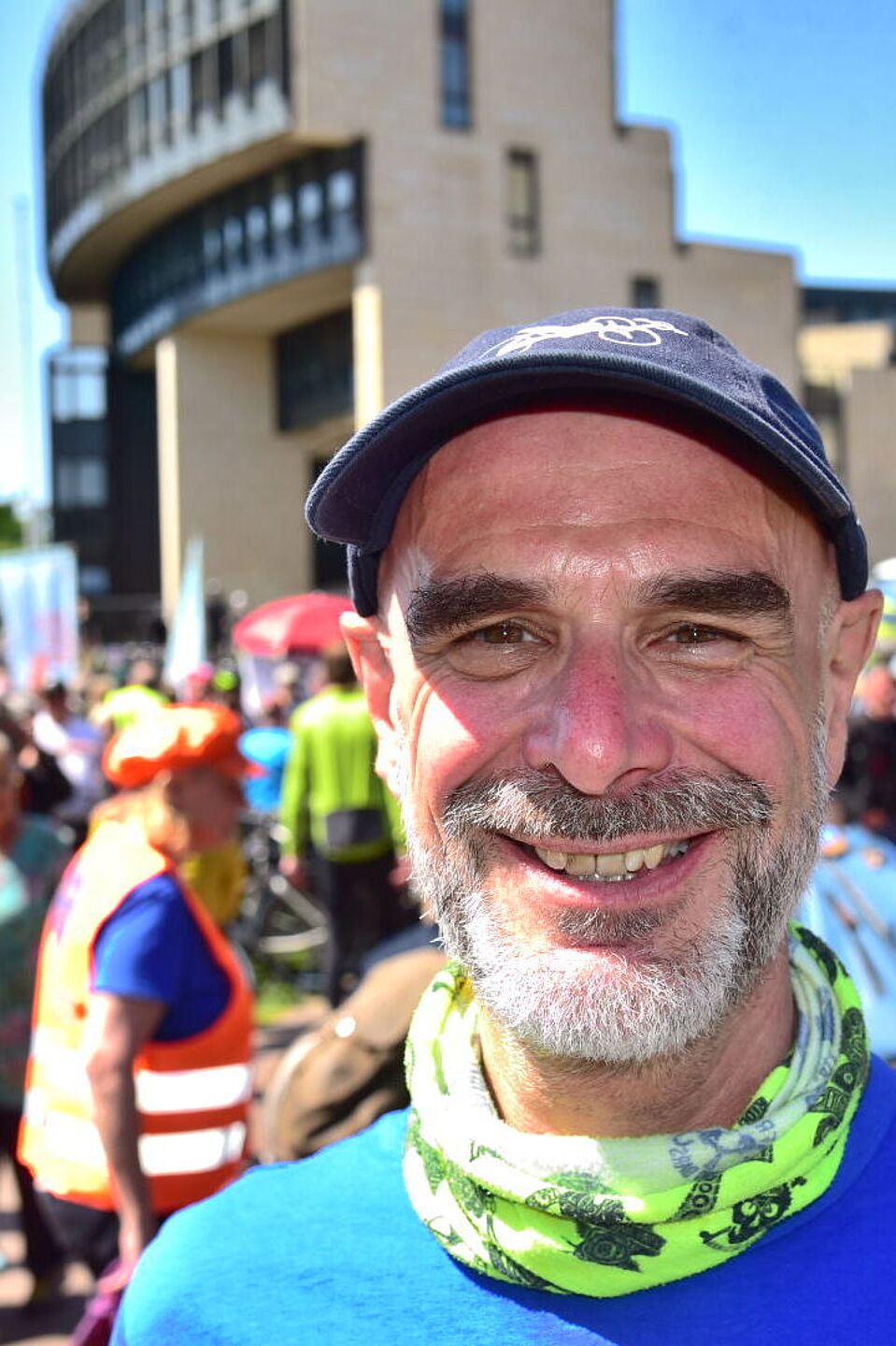 Axel Fell, Landesvorsitzender ADFC NRW  Axel Fell, Landesvorsitzender des ADFC NRW, mit blauem T-Shirt und Mütze bei einer Fahrraddemo mit anderen Radfahrenden im Hintergrund vor dem NRW-Landtag in Düsseldorf.
