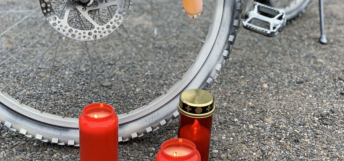 Rote Grabkerzen in Nahaufnahme vor einem Vorderrad eines weiß angemalten Ghost-Bike
